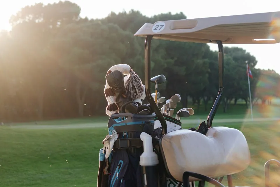 Golf bag with knit headcovers strapped to a golf cart on a sunlit course