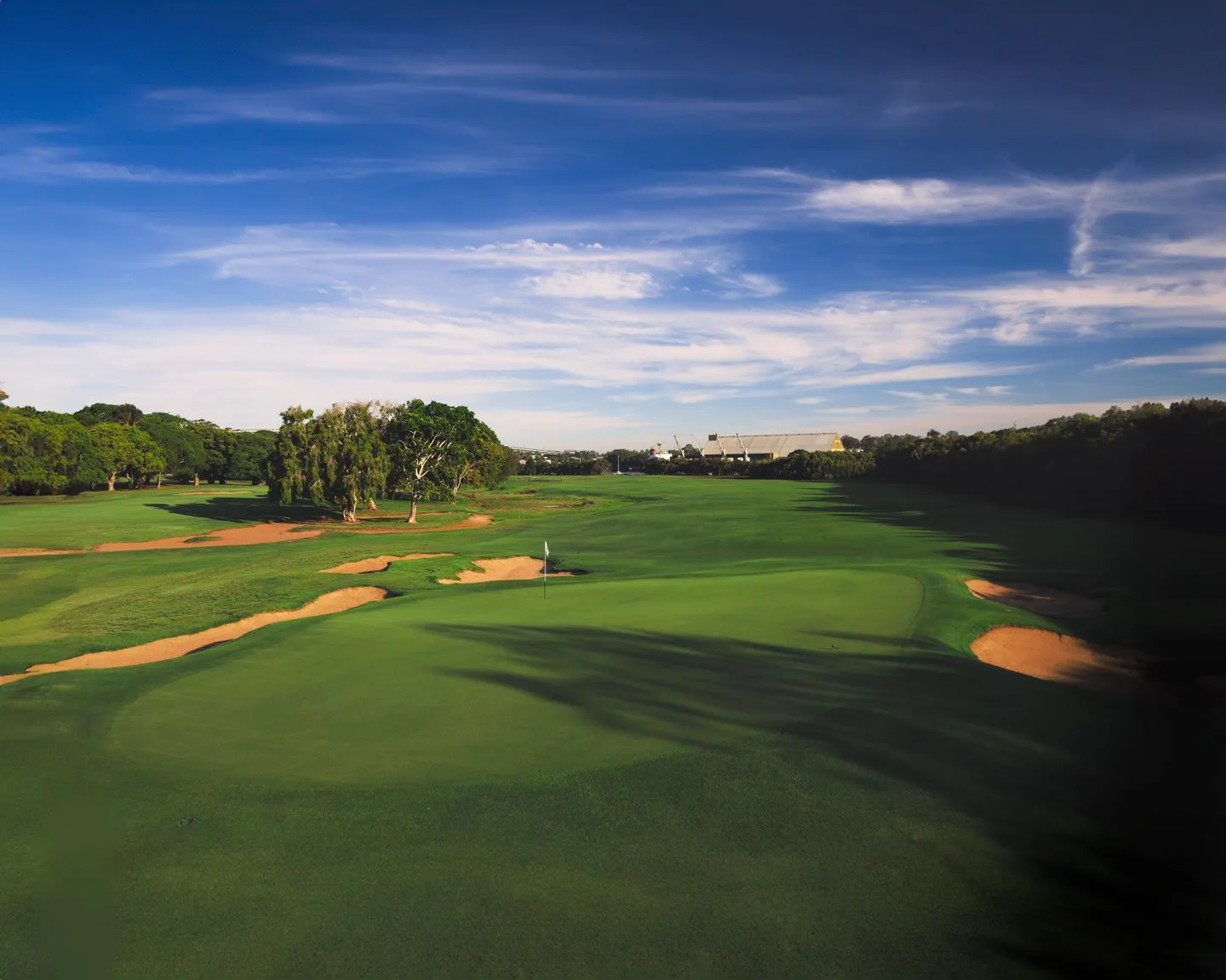 Wide fairway lined with sand bunkers and trees under a deep blue sky