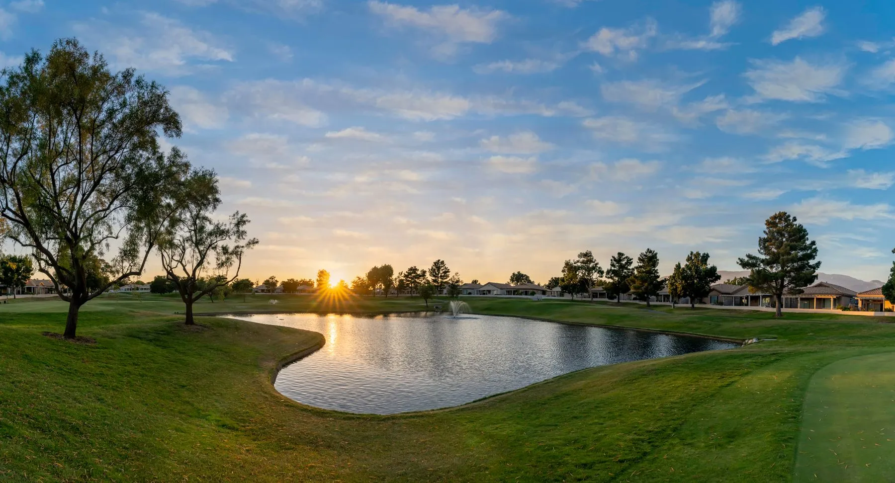 Sun setting over a golf course pond, fairways and trees under a wide sky