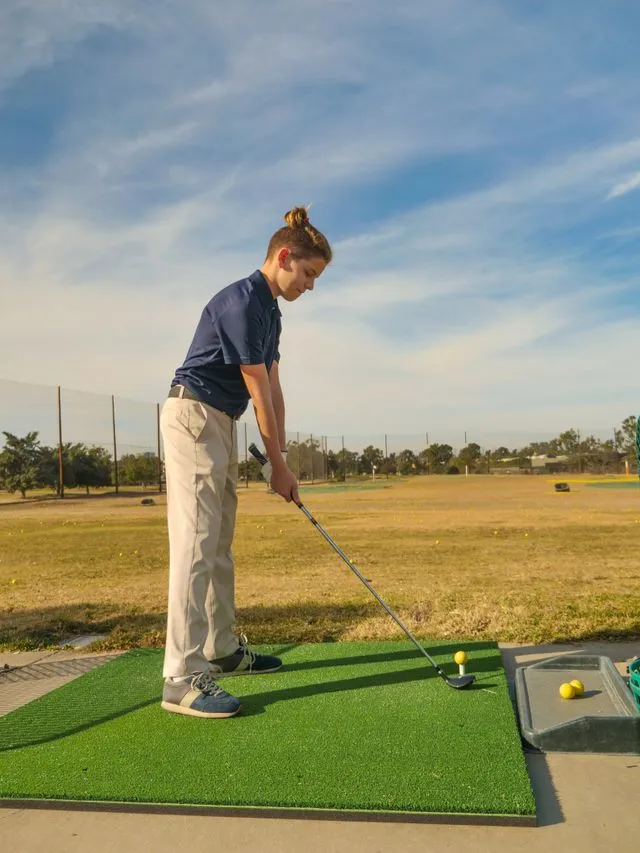 Young golfer addressing a teed-up ball on a driving range mat beside a tray of balls