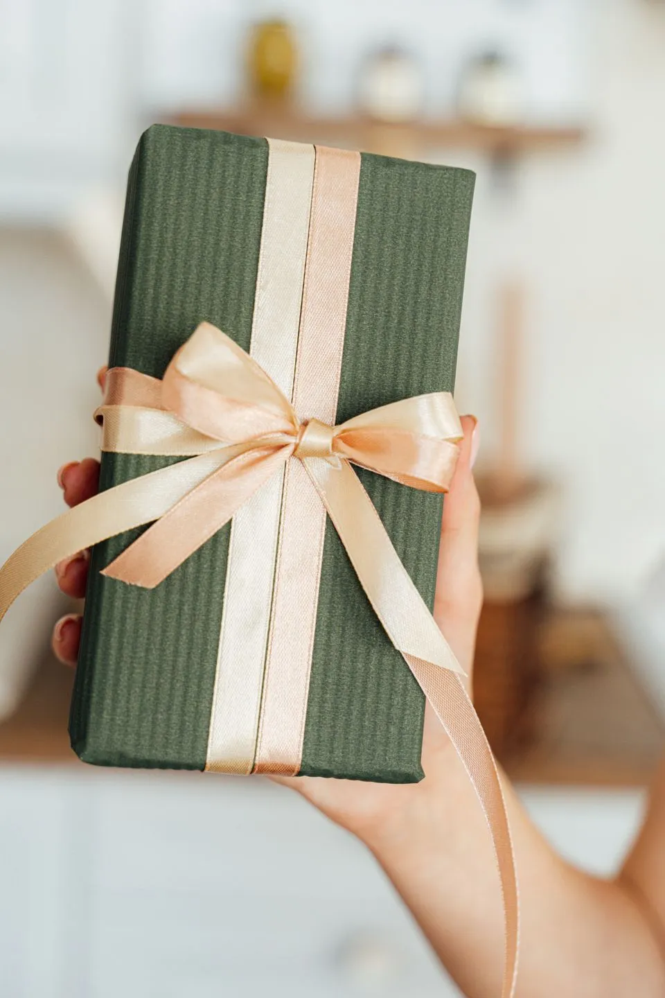 Hand holding a green gift box tied with a peach satin ribbon and bow