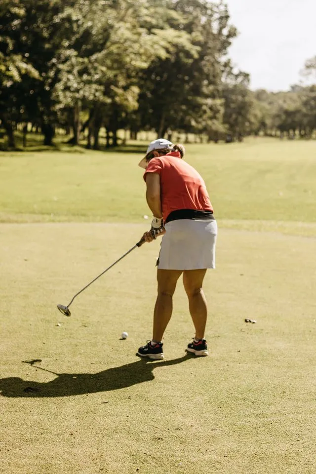 Woman golfer in a red top and white skirt lining up a putt on a sunny course