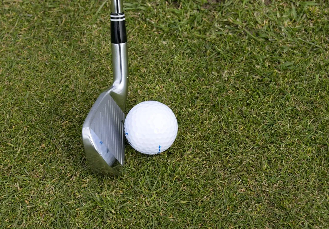 Steel wedge resting beside a white golf ball on short green grass