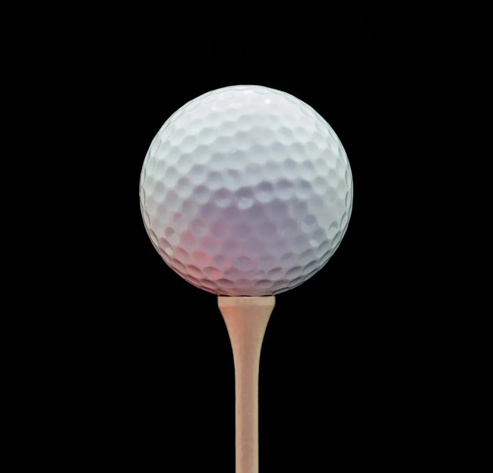Plain white golf ball on a wooden tee against a black background